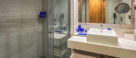 Un baño moderno con cabina de ducha acristalada, un espejo grande y un lavabo blanco.
