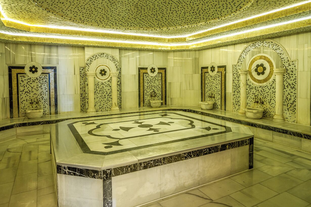 Un vestíbulo lujoso con piso de mármol, decoraciones de pared ornamentadas y un elemento decorativo central.