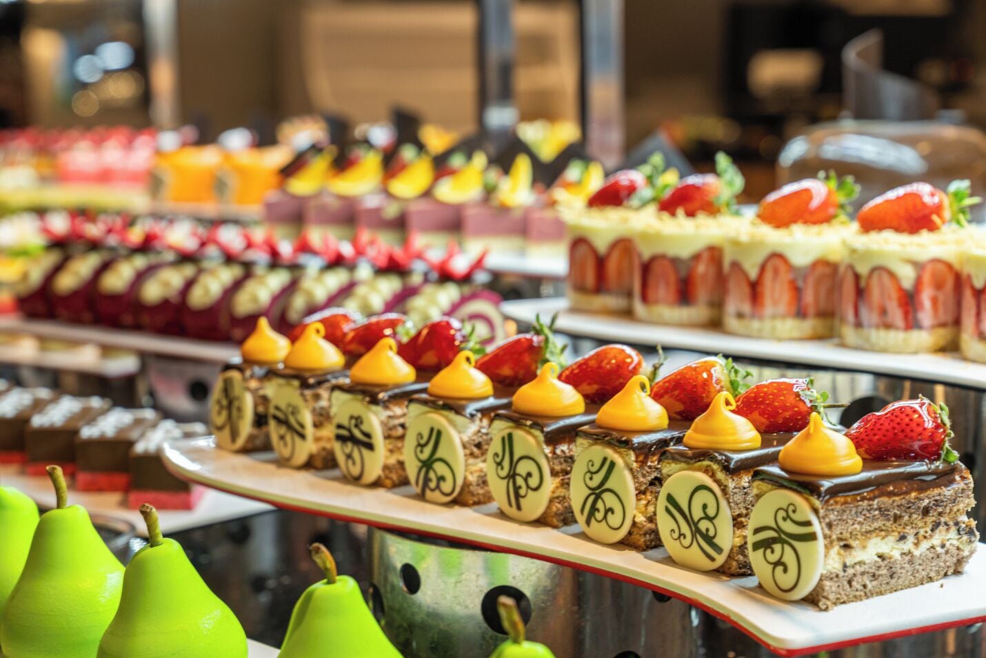 Diversos postres expuestos, como pasteles y hojaldres, adornados con fresas y peras.