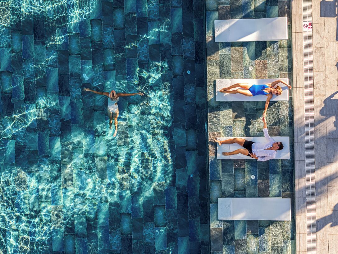 An aerial view of a swimming pool with two lounge chairs and a person swimming.