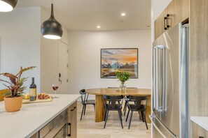 Eine moderne Küche mit einem Holzespeisetisch, schwarzen Stühlen, einem Edelstahlkühlschrank und einem Blumentopf.