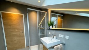 Ein modernes Badezimmer mit Duschkabine aus Glas, einem weißen Waschbecken und einem Holz-Waschtisch.