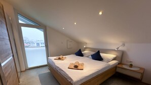 Ein modernes Schlafzimmer mit einem großen Bett, einem Holz-Kopfteil, einem Nachttisch mit Lampe und Blick ins Freie.