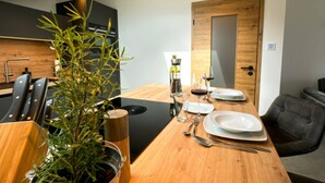 Ein stilvoller Essbereich mit einem Holztisch, gedeckt für zwei Personen, einer Zimmerpflanze und einer Küche im Hintergrund.