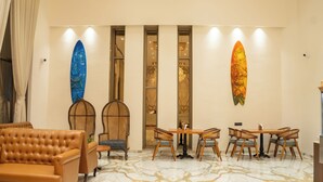 A lobby with a brown sofa, wooden chairs, a marble floor, and surfboards on the wall. - Pride Elite Daman (Daman)