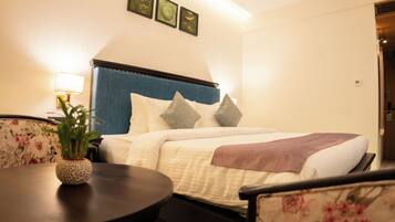A hotel room with a bed, a bedside table with a lamp, a chair, and a small plant.