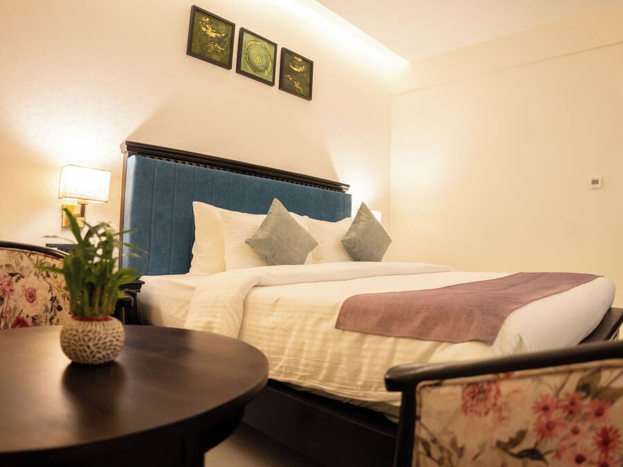 A hotel room with a bed, a bedside table with a lamp, a chair, and a small plant.