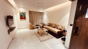A modern living room with a sofa, coffee table, TV, and artwork on the wall. - Pride Elite Daman (Daman)