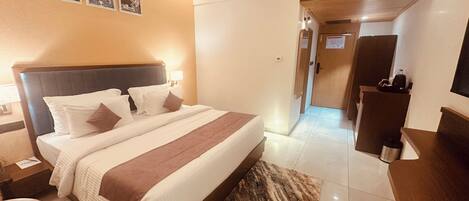 A hotel room with a large bed, bedside tables, a desk, and a mirror.