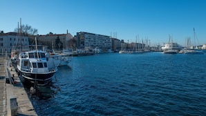 A marina with boats docked along the waterfront, buildings in the background, and a clear blue sky.