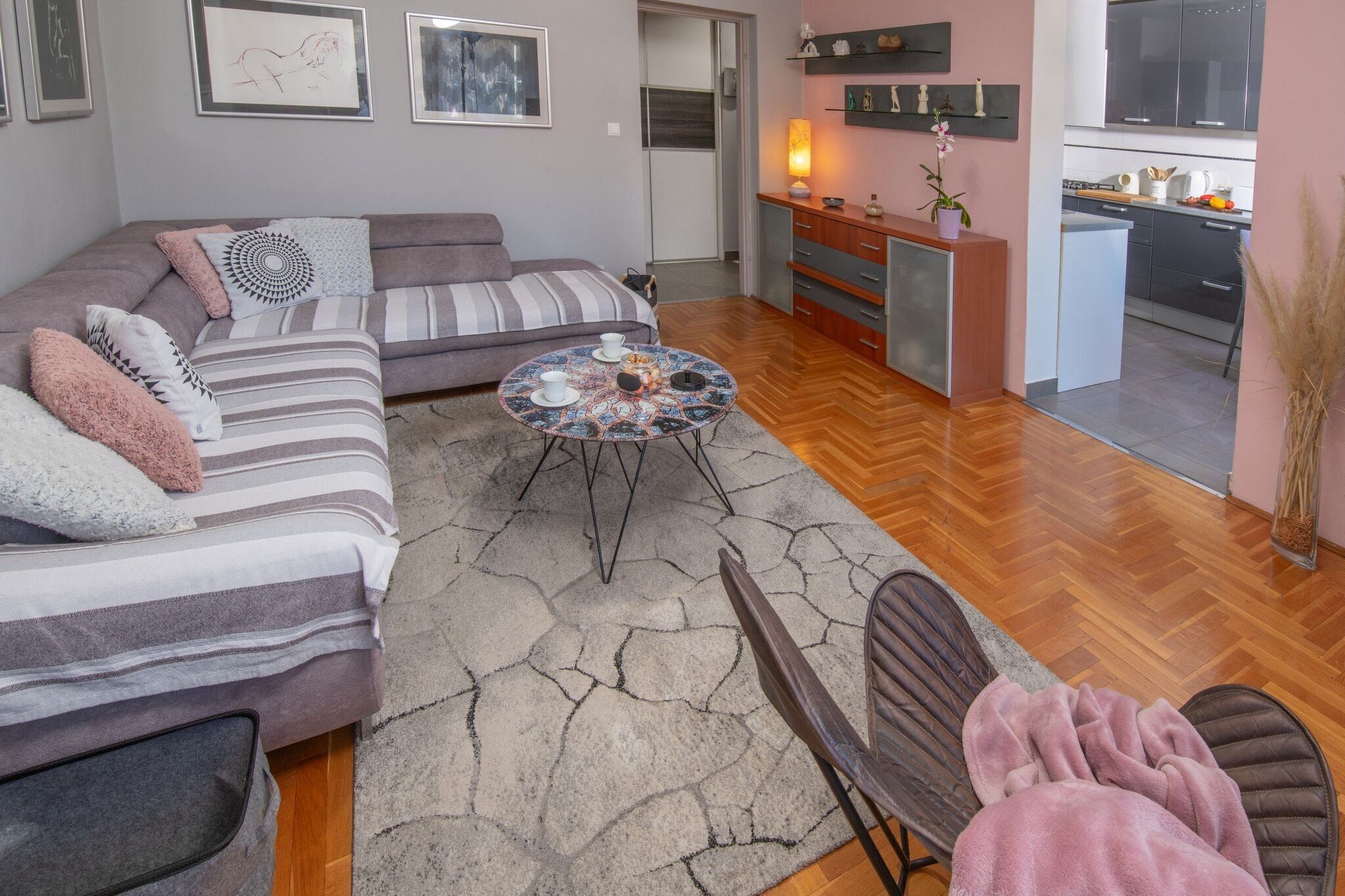A modern living room with a sofa, a coffee table, and a chair. There is a kitchen area with cabinets and a sink visible in the background.
