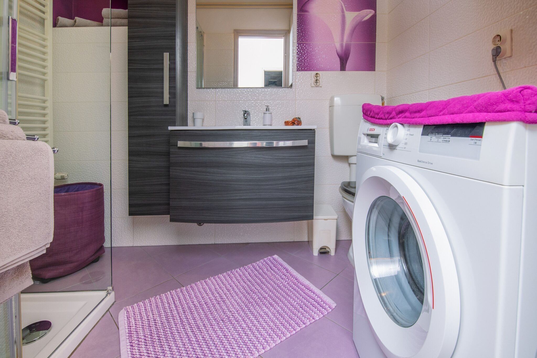 A modern bathroom with a washing machine, a vanity with a mirror, and a shower area.