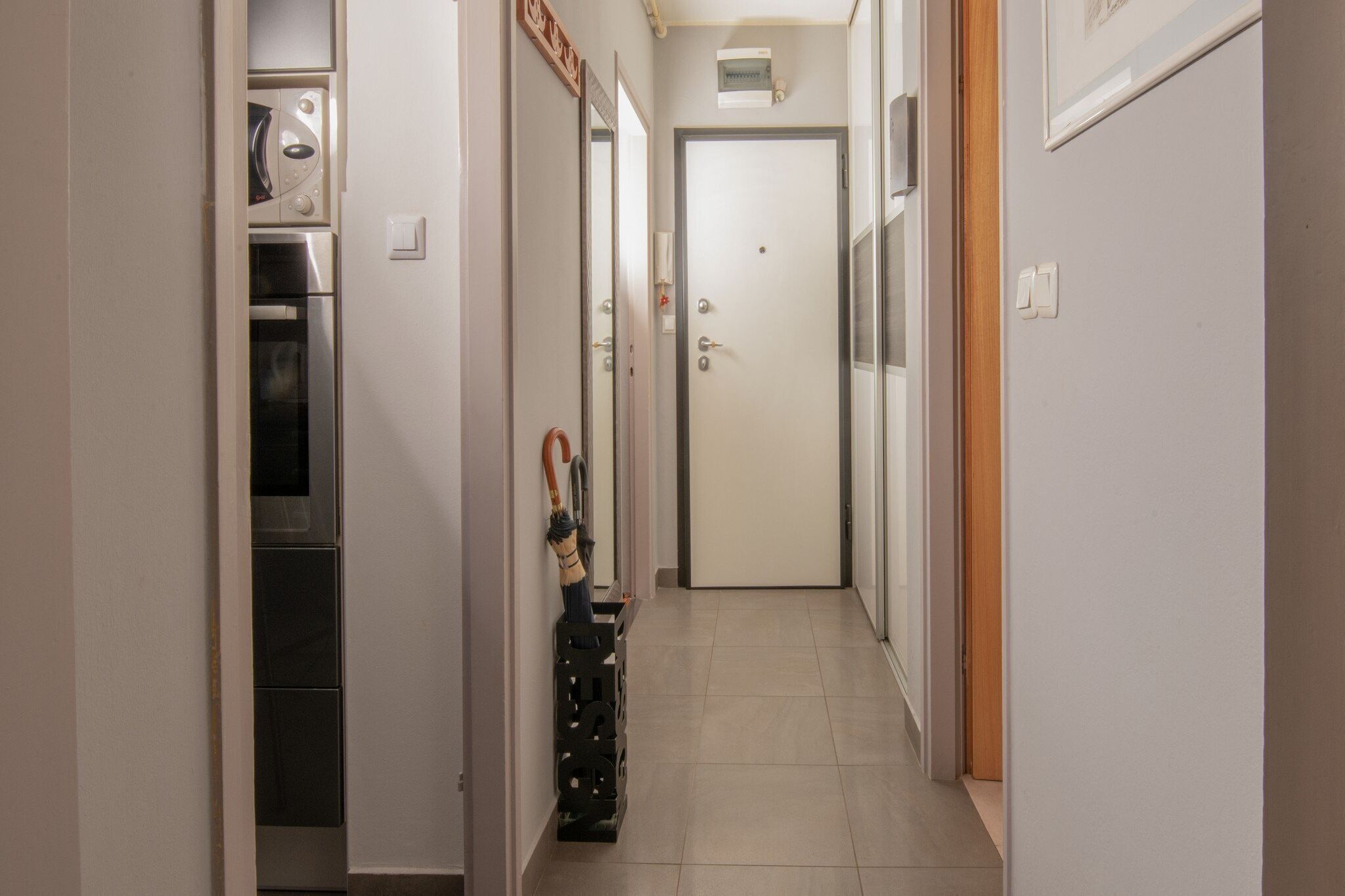 A narrow hallway with a kitchen area on the left, a door at the end, and a broom leaning against the wall.