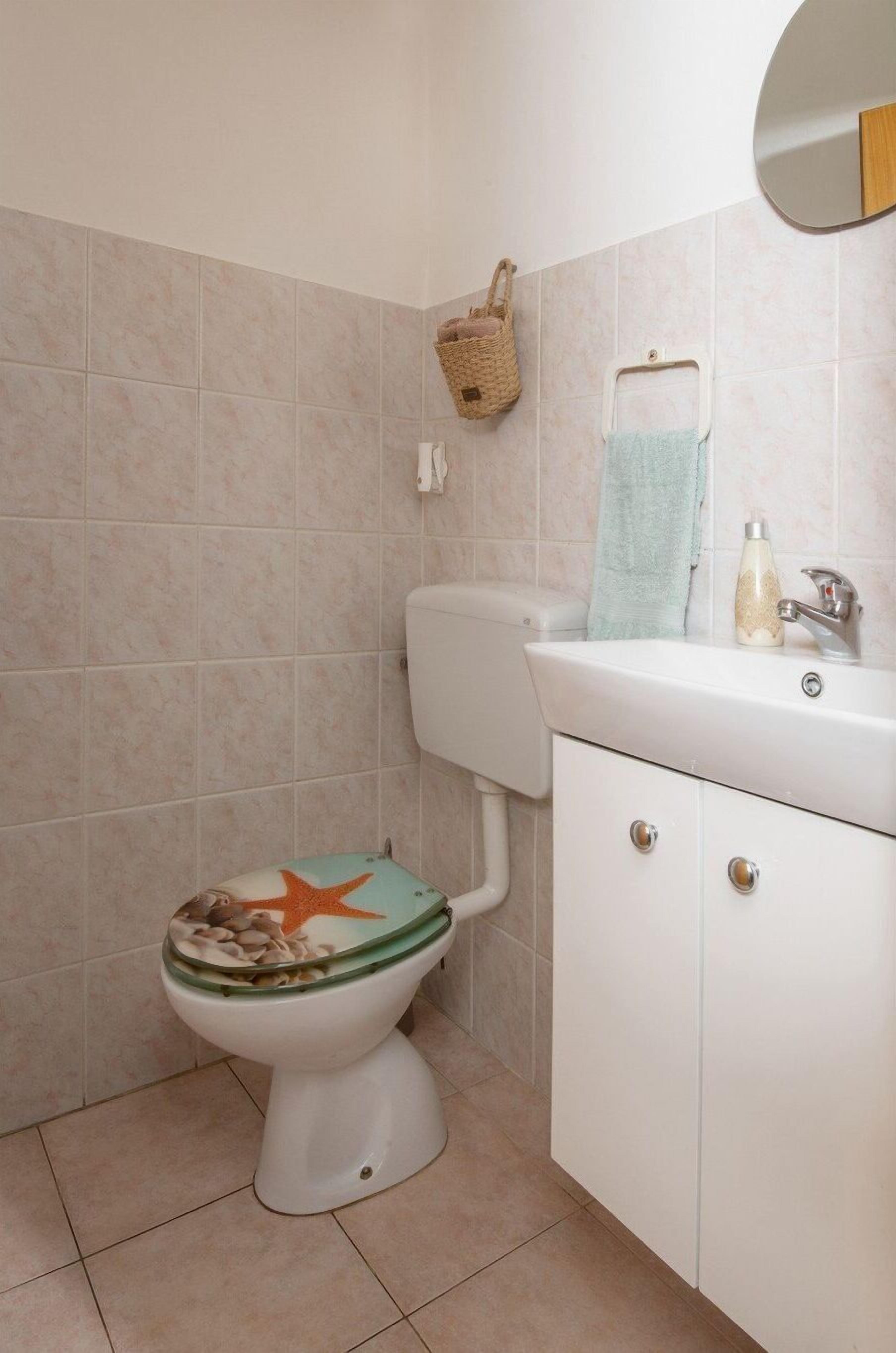A bathroom with a toilet, a sink, a mirror, and a small basket on the wall.