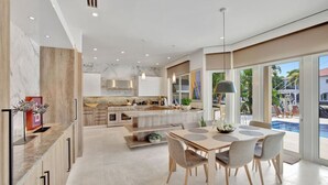 Une cuisine moderne dotée d’un îlot central, de grandes fenêtres et d’un coin repas avec vue sur la piscine.