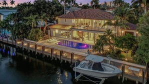 Une propriété située au bord de l’eau, comprenant une grande maison, une piscine et un quai avec un bateau.