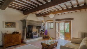 A rustic living room with exposed wooden beams, a fireplace, a glass coffee table, and a sofa. - Stunning private villa for 8 people with WIFI, private pool, A/C, TV and panoramic view (Cortona)