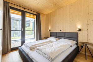 A bedroom with two beds, a wooden ceiling, and a view through a glass door.