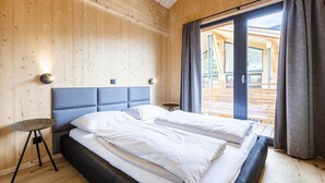 A modern bedroom with a large bed, wooden walls, and a view of the outdoors.