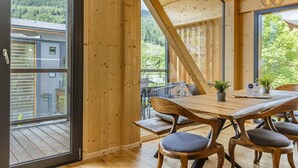 A wooden interior with a large window, a dining table, and chairs.