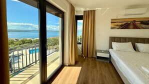 A hotel room with a large sliding glass door leading to a balcony with a pool, a bed with white linens, and a painting on the wall. - Apartment in Croatia near the Adriatic Coast (Crikvenica)