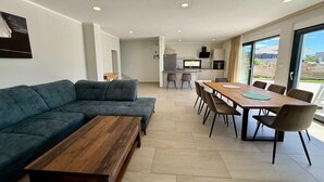 A modern living room with a sectional sofa, a wooden coffee table, and a dining area with a long table and chairs. - Apartment in Croatia near the Adriatic Coast (Crikvenica)