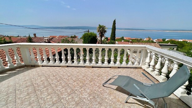 Un balcone con vista sul mare, ringhiere bianche e una sola poltrona da relax.