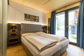 Un dormitorio con cama doble, dos mesitas de noche, una lámpara de pared y un amplio ventanal con cortinas.