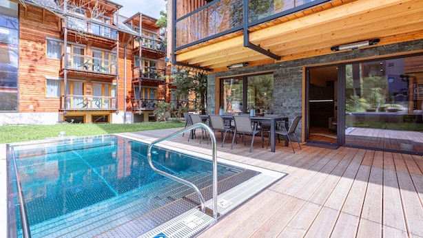 A modern building with a wooden deck, a swimming pool, and outdoor furniture.