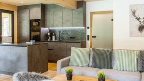 A modern kitchen with a central island, built-in appliances, and a grey sofa with patterned cushions.