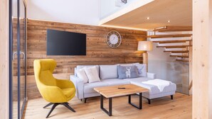 Una sala de estar moderna con un sofá, un sillón amarillo, una mesita de centro, un televisor montado en la pared y una escalera.