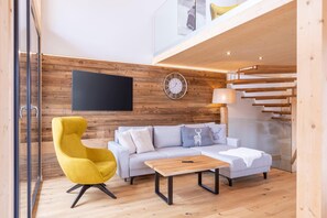 A modern living room with a sofa, a yellow armchair, a coffee table, a wall-mounted TV, and a staircase.