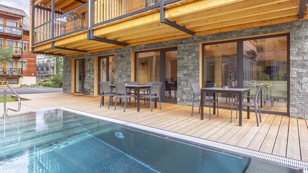 Ein modernes Gebäude mit einer Holzdiele, einem Pool und einem Essbereich im Freien.