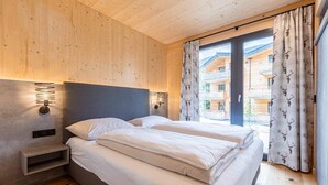 Ein Schlafzimmer mit Holzboden, einem Bett mit weißer Bettwäsche, einem Nachttisch, einer Wandleuchte und einem Fenster mit Vorhängen.
