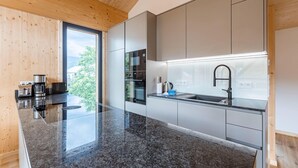 Une cuisine moderne dotée d’un plan de travail en granit, d’appareils électroménagers en acier inoxydable et d’une grande fenêtre donnant sur un paysage verdoyant.
