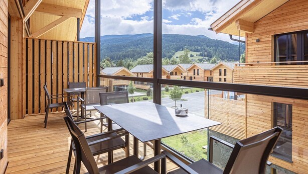 Une cabane en bois dotée d’un balcon, d’une table et de chaises, qui offre une vue sur une vallée où se trouvent d’autres cabanes.
