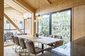 Enjoy meals in this spacious dining area with a long table and six chairs, surrounded by high ceilings and large windows offering views of the surrounding landscape.
