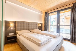 Un dormitorio con una cama grande, lámparas de noche y vista a un edificio de madera a través de un vidrio.