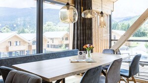 Ein Essbereich mit einem Holztisch, grauen Stühlen und hängenden Pendelleuchten. Auf dem Tisch steht eine Vase mit Blumen.