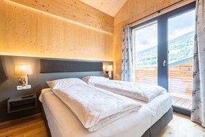 Une chambre à coucher avec un lit, des lampes de chevet, une table de nuit et une vue sur un paysage montagneux, visible à travers une grande fenêtre.