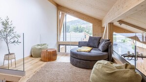 Un dormitorio tipo loft acogedor, con un tragaluz grande, un sofá gris cómodo, una mesita de madera y una planta en maceta.