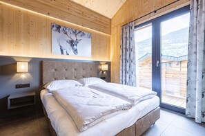 A bedroom with a large bed, a headboard, two bedside lamps, a wall-mounted artwork, and a sliding glass door leading to an outdoor area.