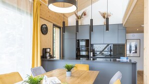 Una cucina moderna con isola centrale, luci a sospensione e zona pranzo con tavolo e sedie in legno.
