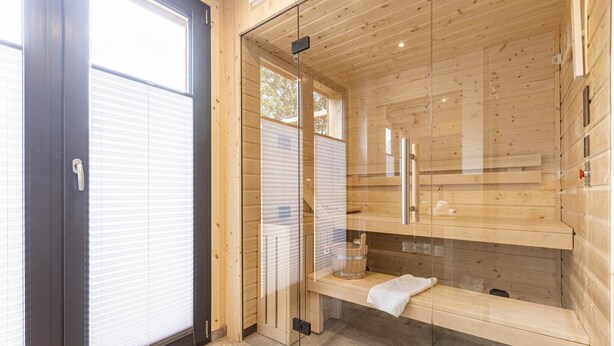 Una sauna con pareti in legno, una porta in vetro, una panca e un porta asciugamani.