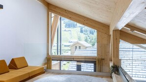 Una camera moderna con una grande finestra, travi in legno, un divano e un tappeto rotondo.