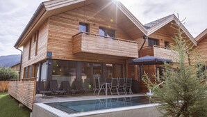 Een houten chalet met een balkon, zwembad en buitenmeubilair.