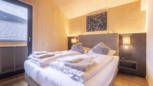Una habitación de hotel moderna con dos camas, un ventanal grande, paredes de madera y vistas a las montañas.
