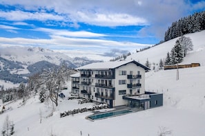 Ein modernes Mehrstöckhotel mit Balkonen, einem Schwimmbad und Blick auf verschneite Berge.