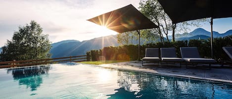 A swimming pool with clear water, surrounded by lounge chairs and a wooden fence, with mountains in the background.