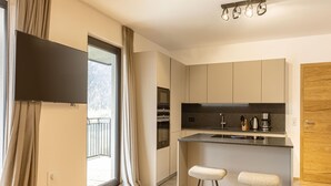 Una cocina moderna con una isla grande, taburetes de bar, un televisor de pantalla plana y una puerta corrediza de vidrio a un balcón.